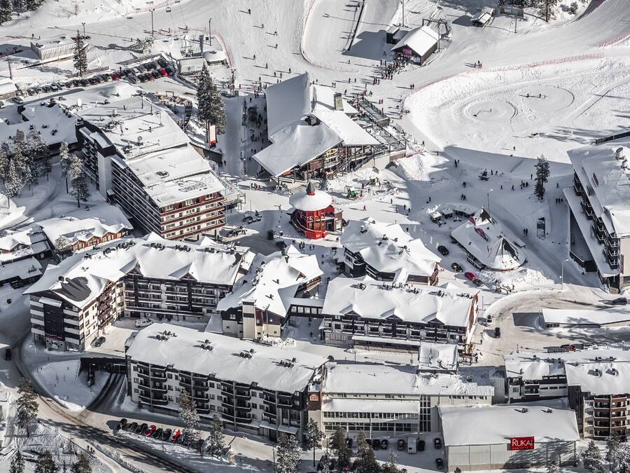 A snow-covered ski resort with multiple buildings, including a prominent red structure, and a winding ski slope.