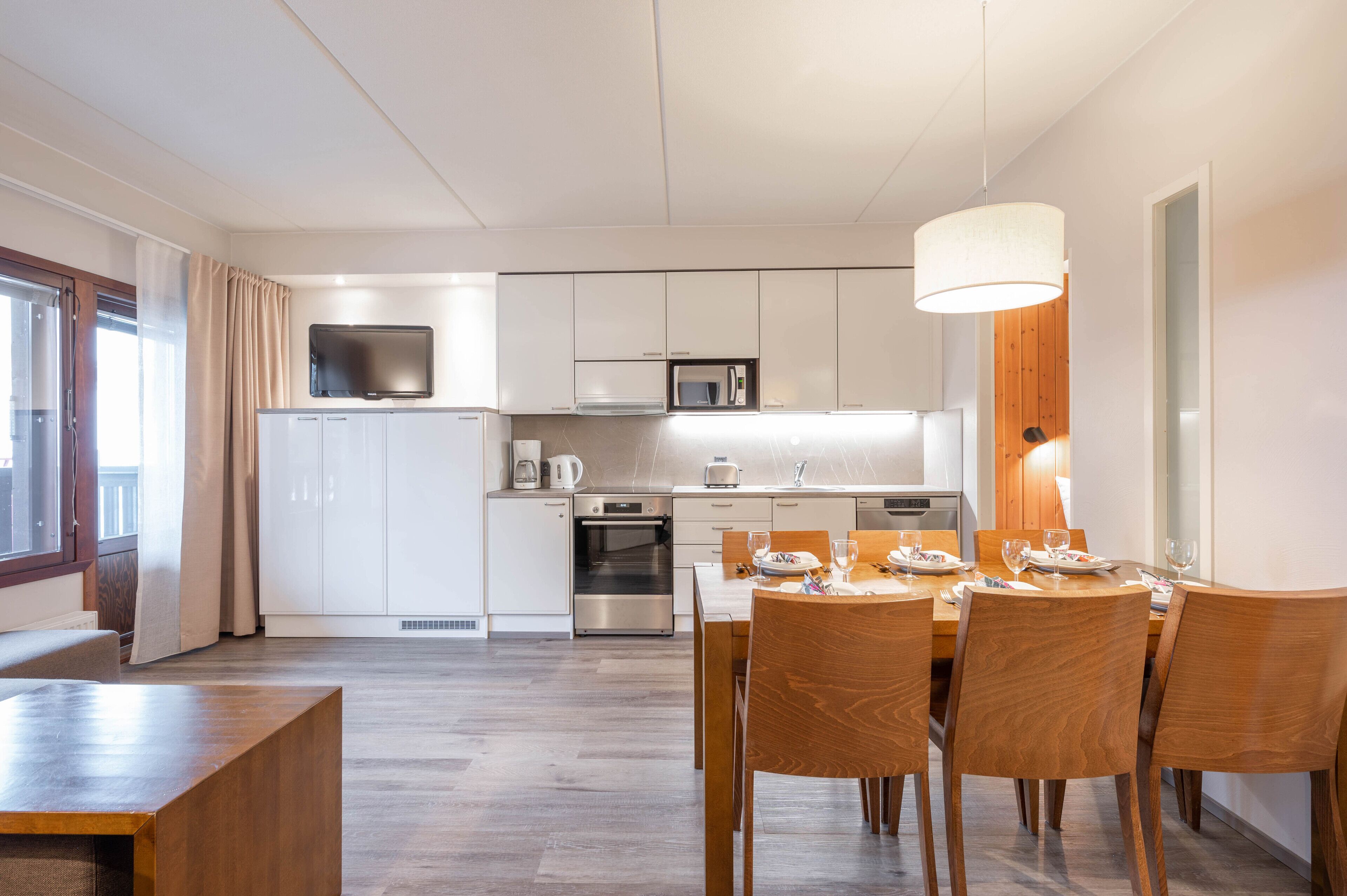 A modern kitchen with white cabinets, a microwave, and a dining area with wooden chairs and a table set for four.