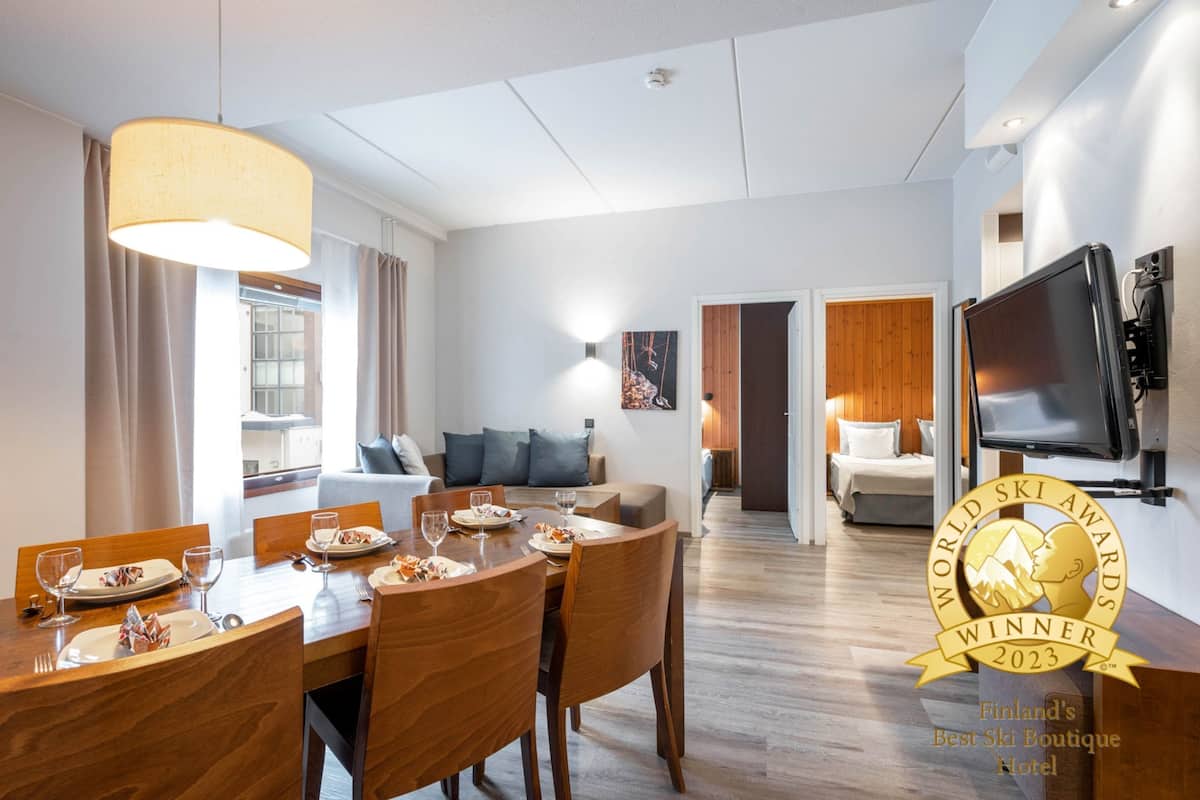 A hotel room with a dining area, a living room, and a TV mounted on the wall.