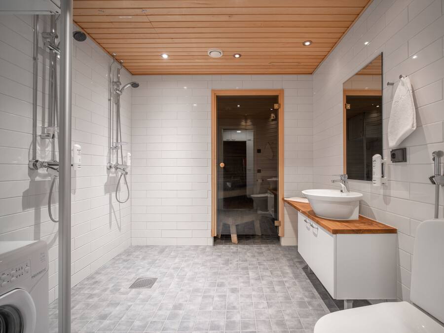Un baño moderno con cabina de ducha de vidrio, techo de madera y lavabo blanco sobre encimera de madera.