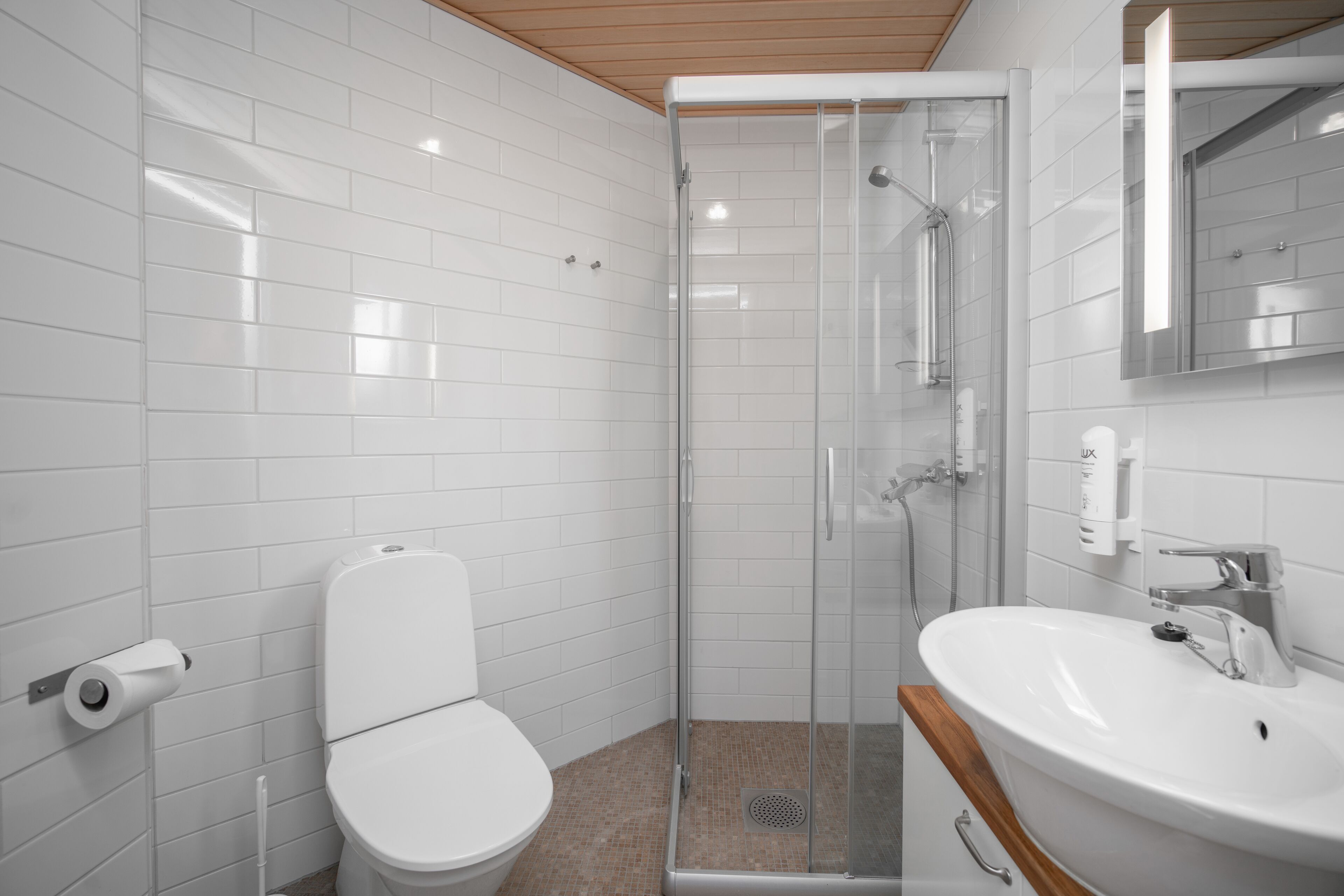 A modern bathroom with white tiles, a glass-enclosed shower, a white toilet, and a sink with a mirror above it.