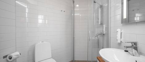 A modern bathroom with white tiles, a glass-enclosed shower, a white toilet, and a sink with a mirror above it.