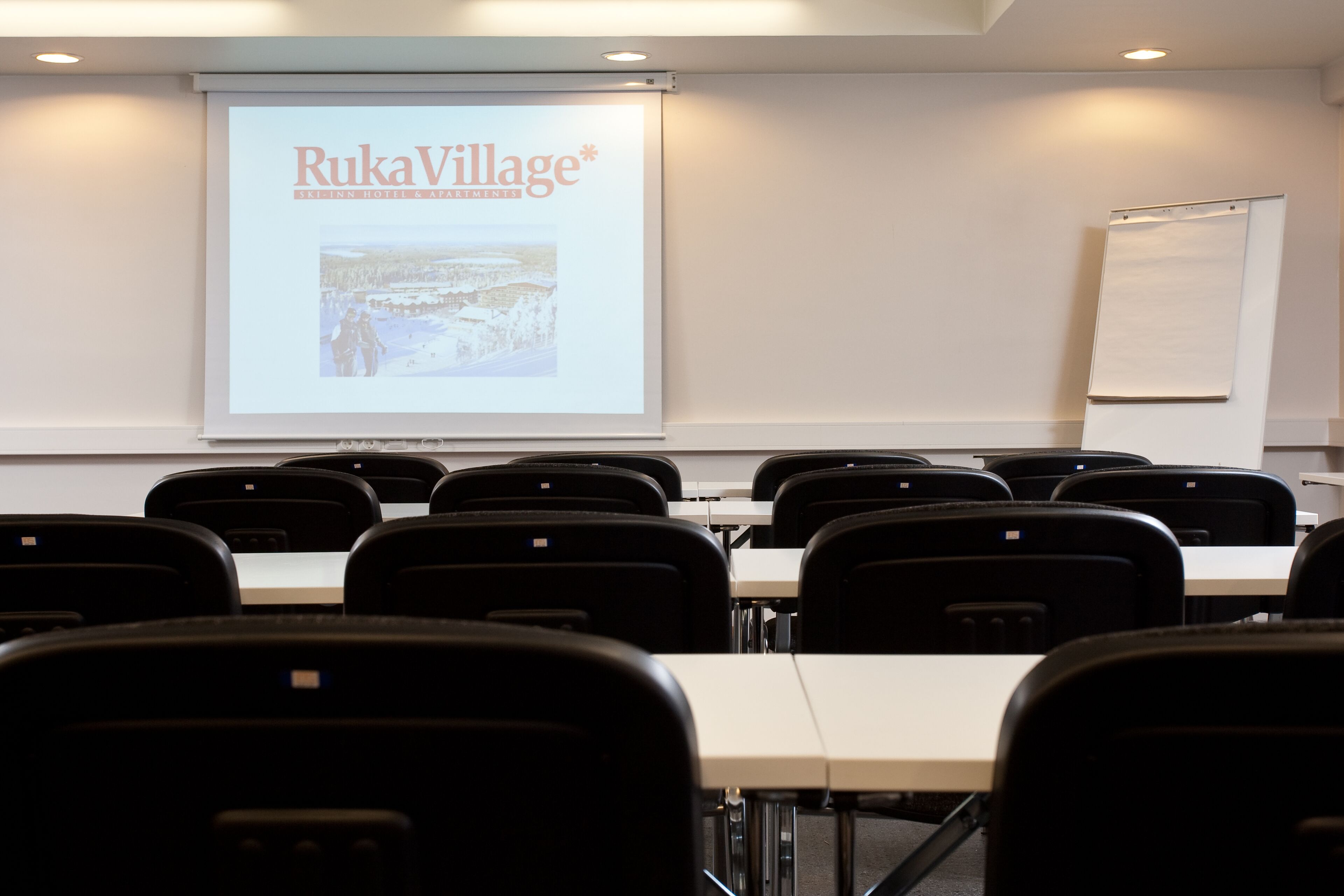 A conference room with a presentation screen displaying 'RukaVillage' and a whiteboard.