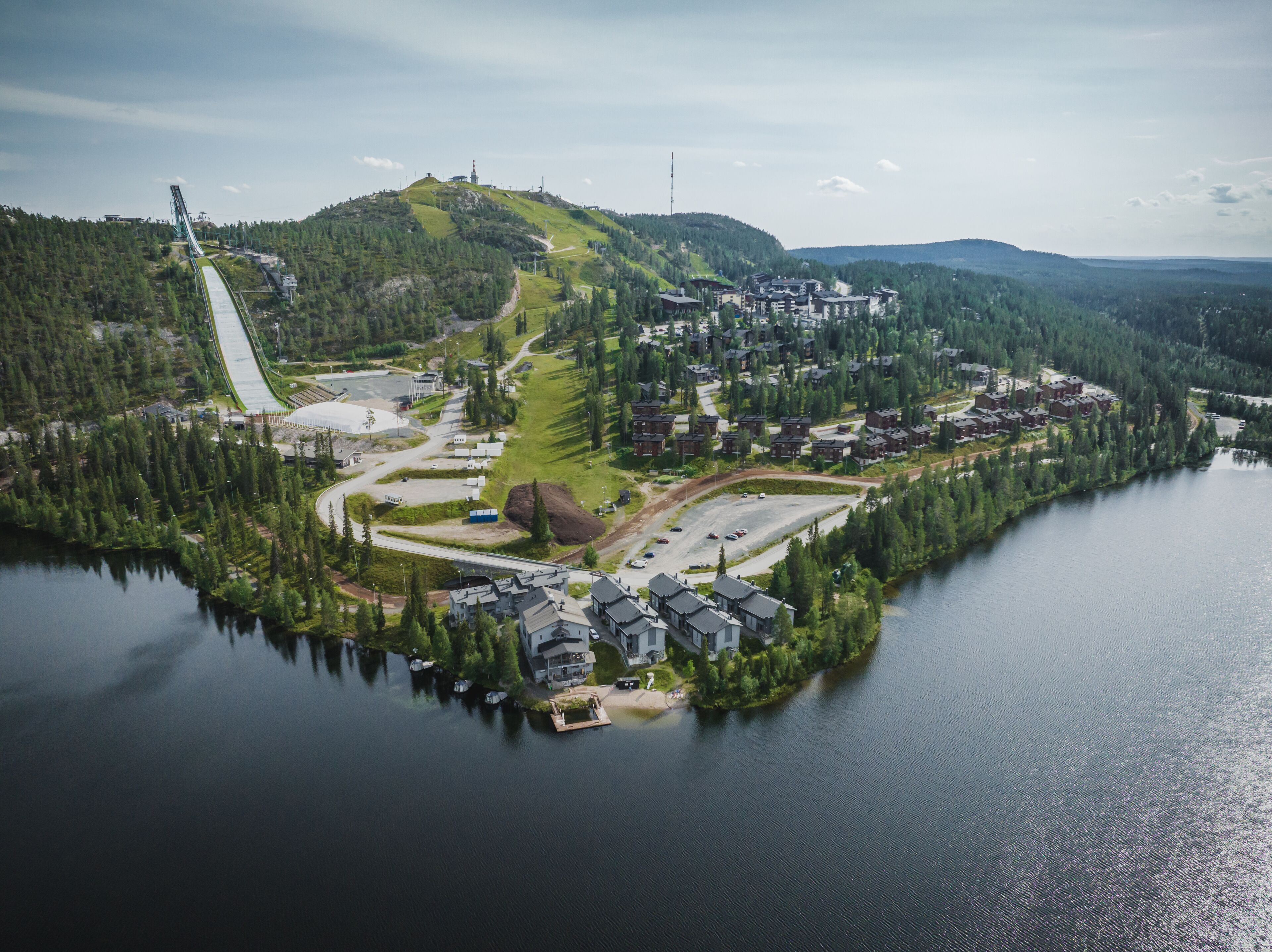 An aerial view of a lakeside residential area with houses, a dock, and a ski lift.