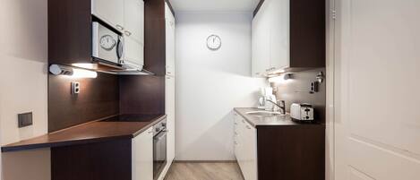 Una cocina compacta con armarios de madera oscura, horno empotrado, microondas y tostadora.