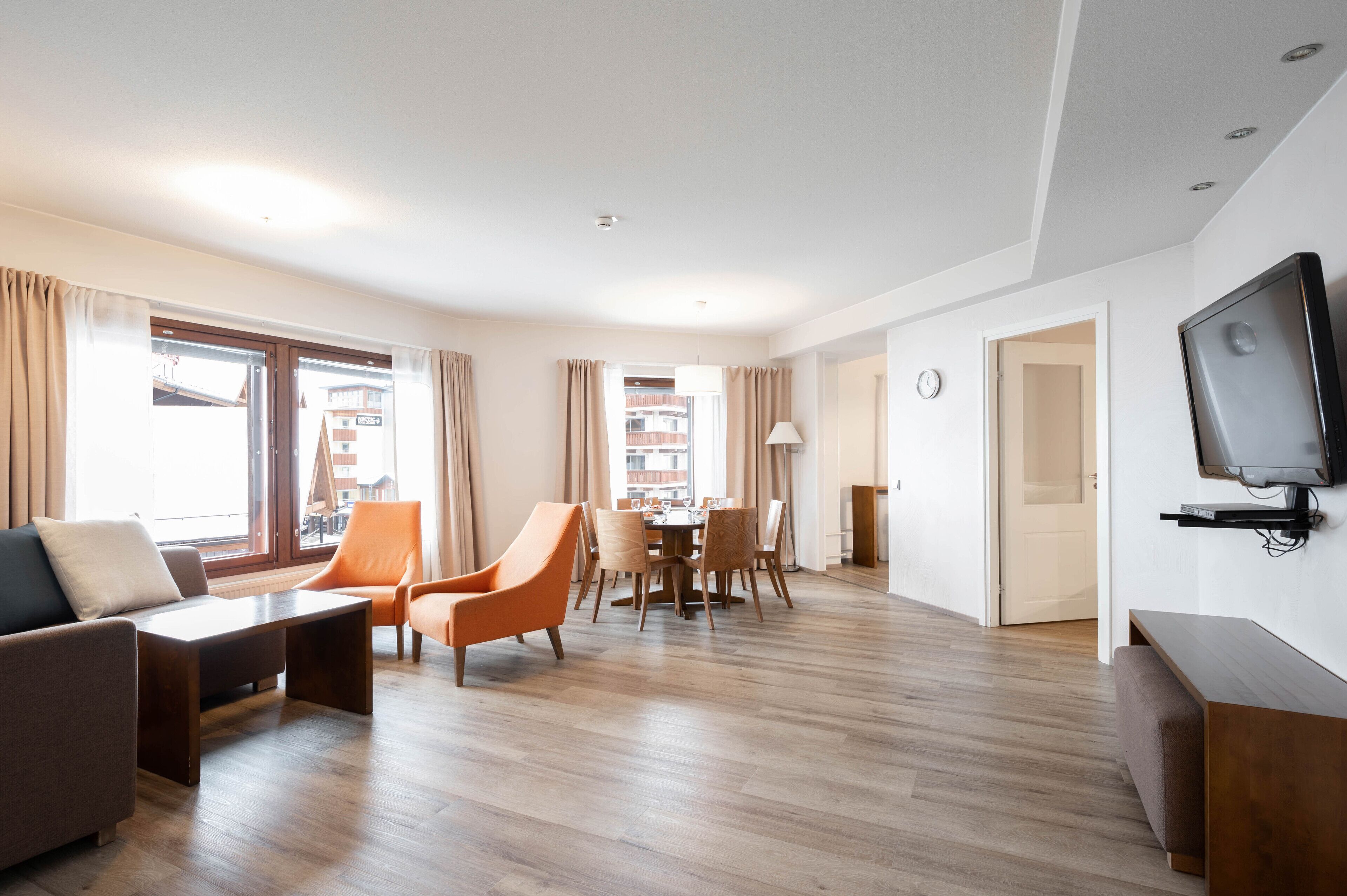 Una sala de estar moderna con un sofá, sillones, una mesa de comedor y un televisor montado en la pared.