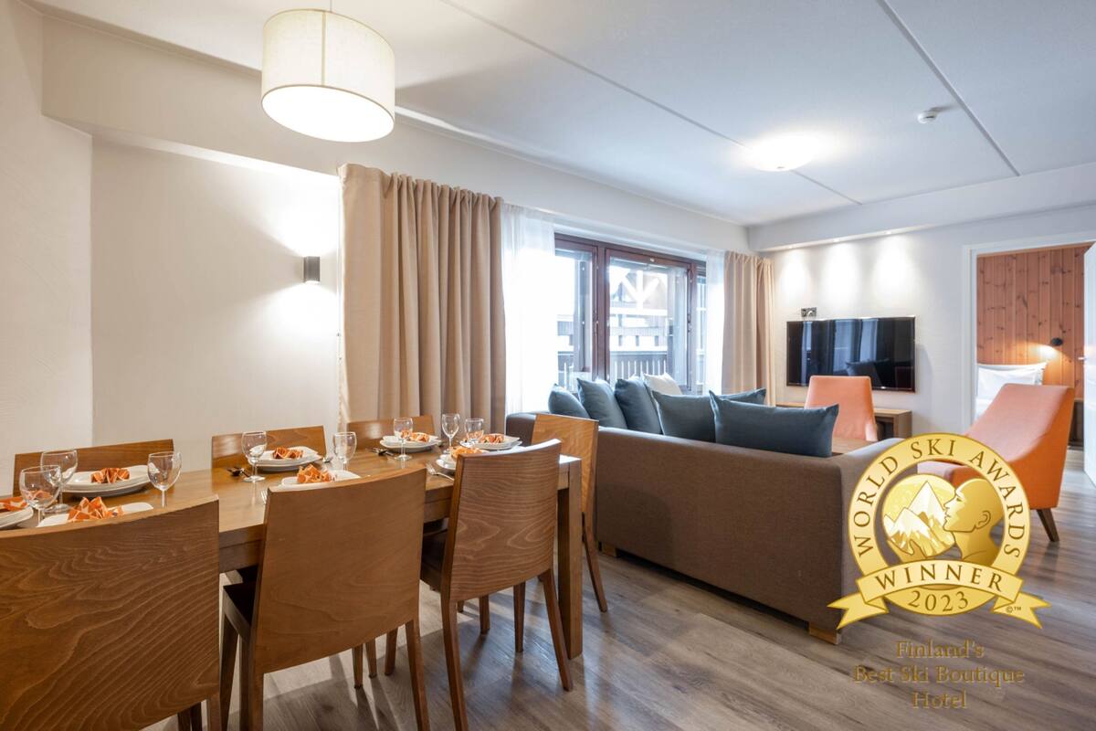A modern hotel room with a dining area, a sofa, and a TV. It is labeled as the World Ski Awards Winner 2023.