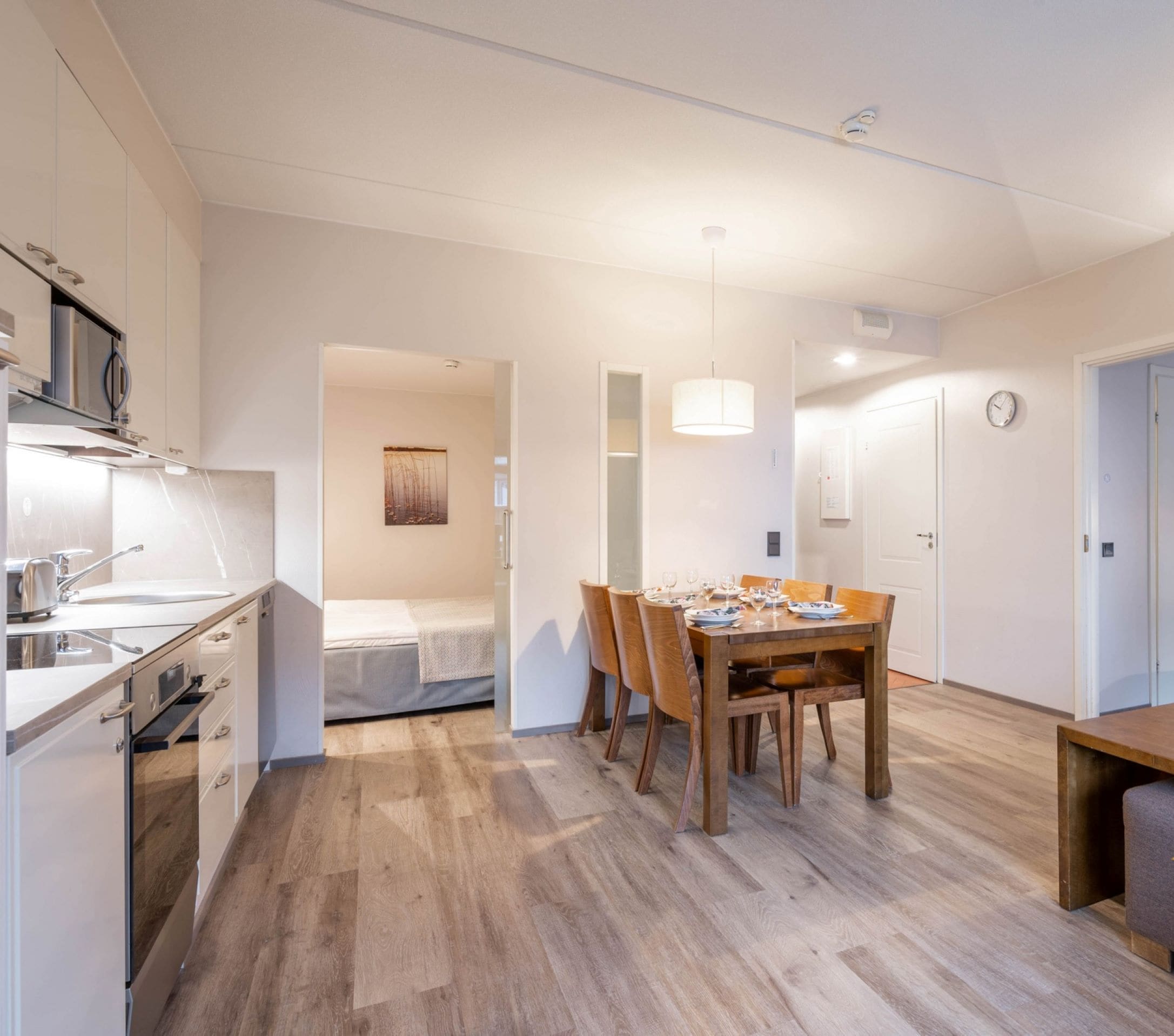 Quarto de hotel moderno com cozinha compacta, área de refeições com mesa e cadeiras de madeira, um sofá e uma cama.