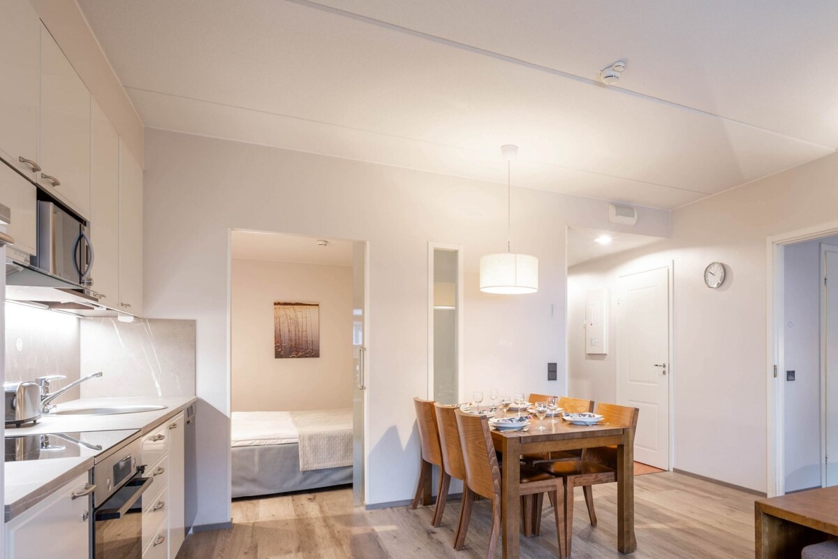 Une chambre d’hôtel moderne dotée d’une kitchenette, d’un coin repas avec une table et des chaises en bois, d’un canapé et d’un lit.