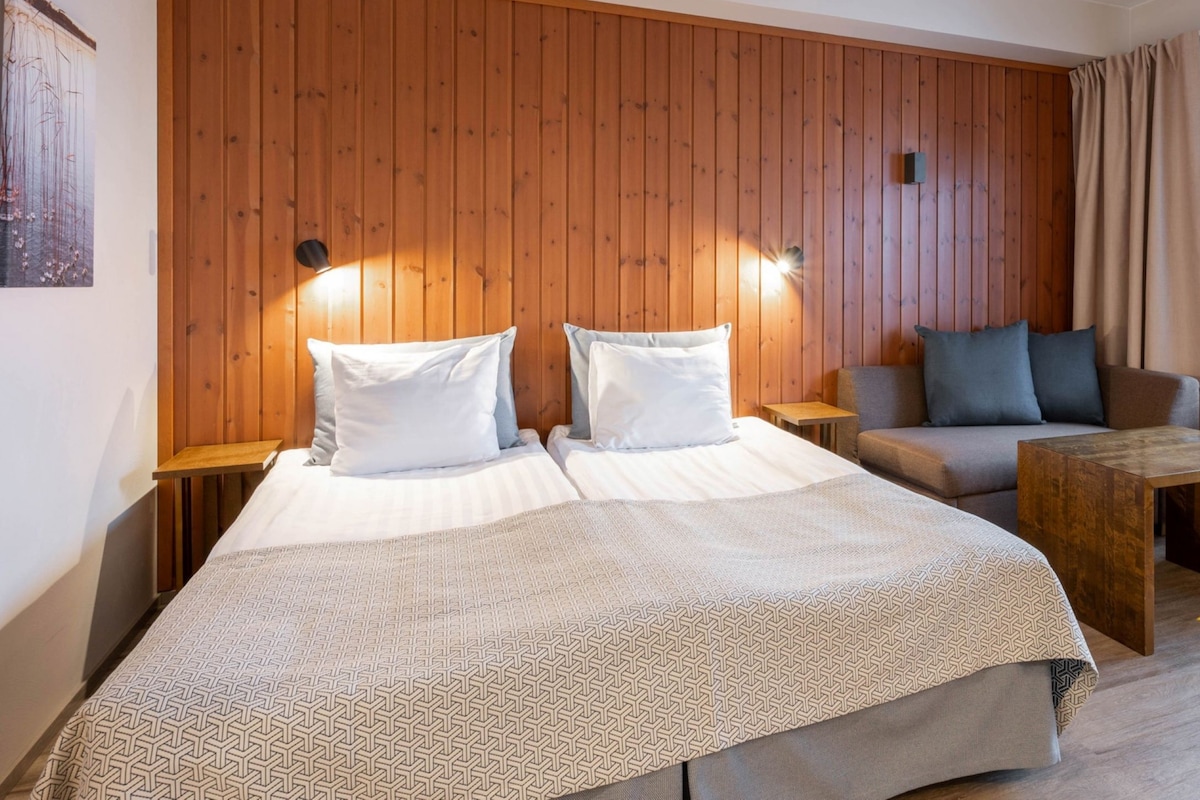 Une chambre d’hôtel avec un mur lambrissé en bois, un grand lit avec deux oreillers, un canapé, une petite table et une fenêtre avec des rideaux.