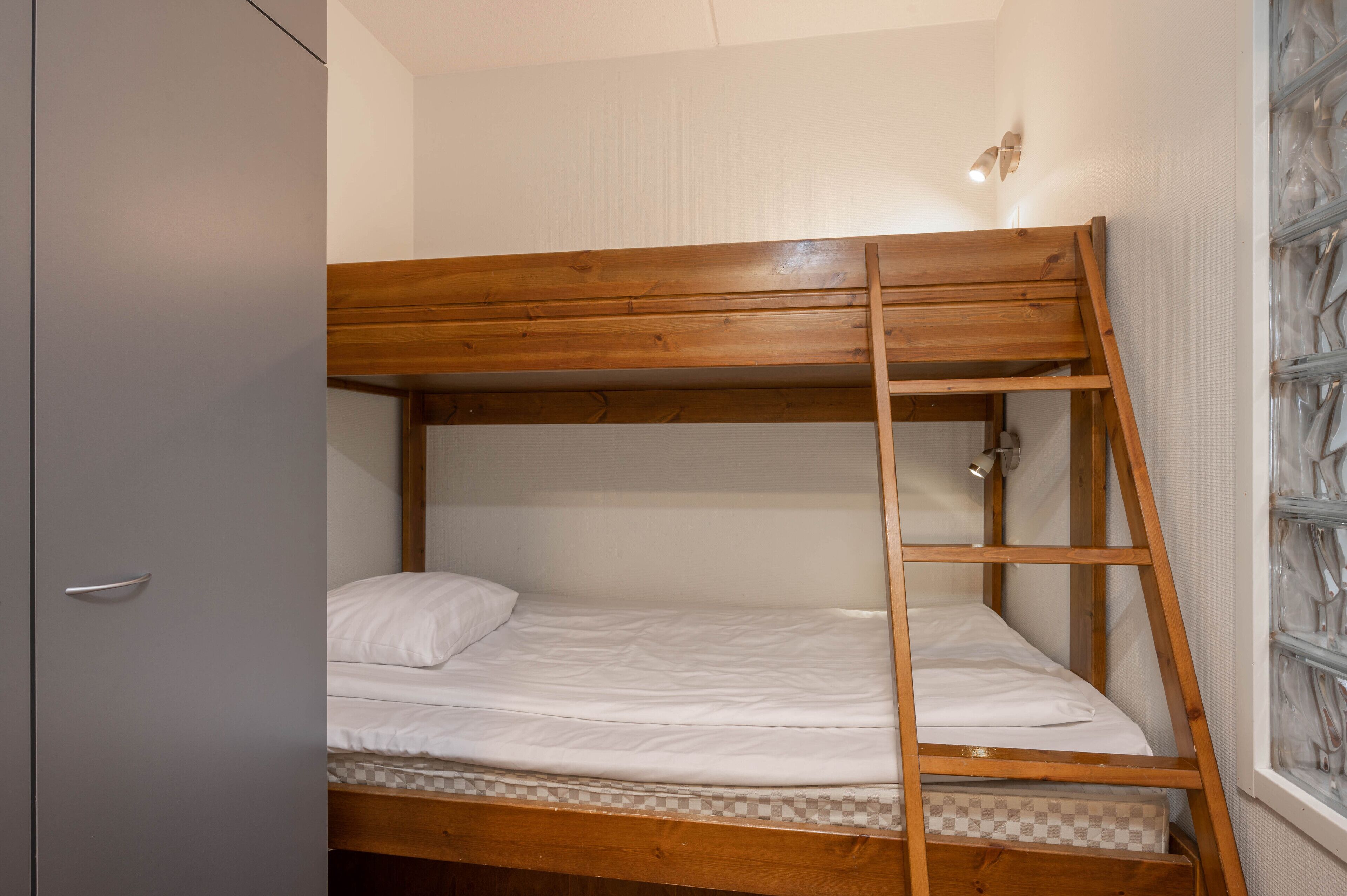 A bunk bed with a wooden ladder, a white mattress, and a checkered mattress cover.