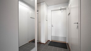 Käytävä, jossa on laatoitettu lattia, valkoiset ovet ja musta ovimatto.