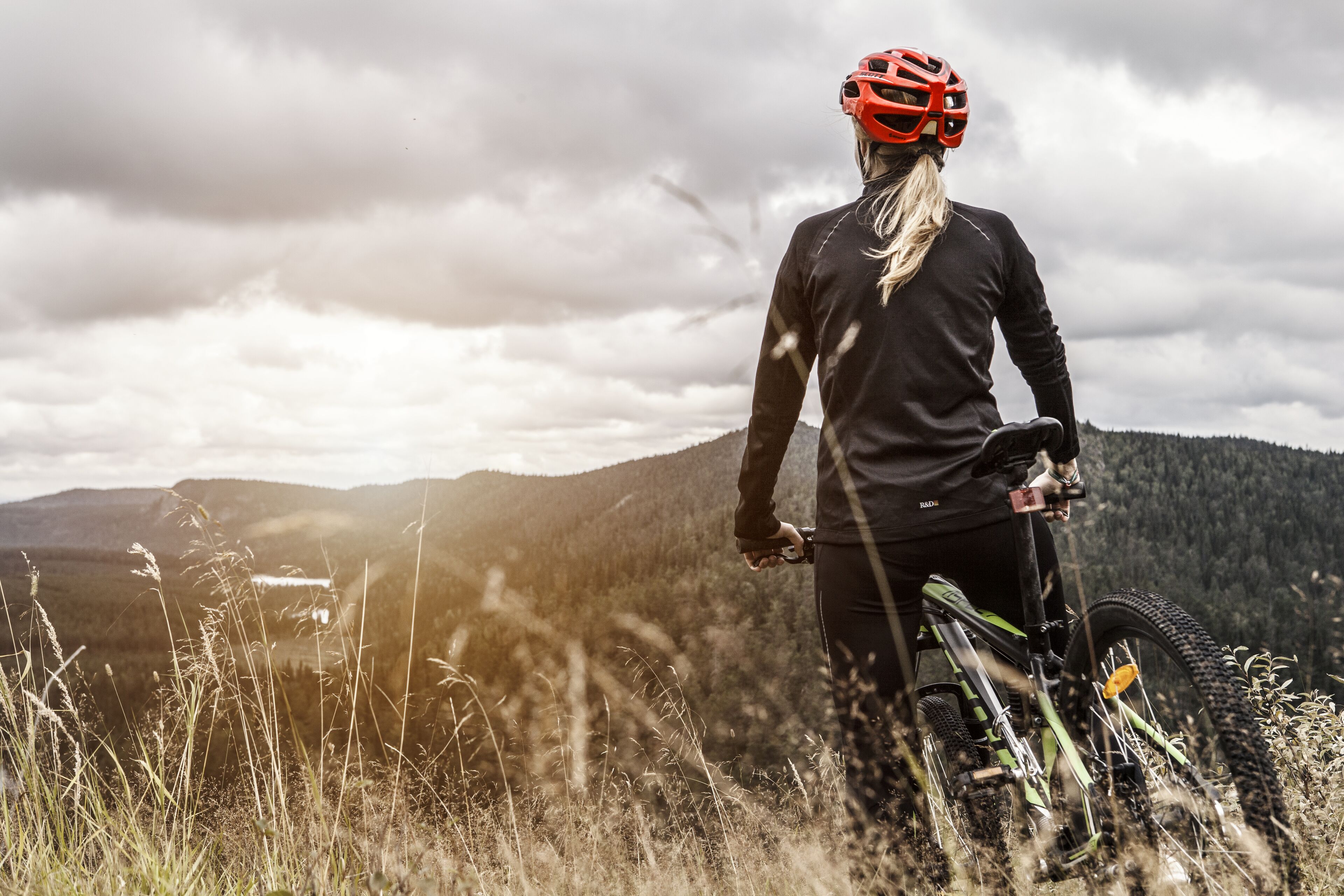 A mountain biker on a trail with a view of a forested mountain range in the background.