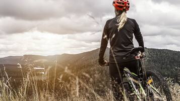 A mountain biker on a trail with a view of a forested mountain range in the background.