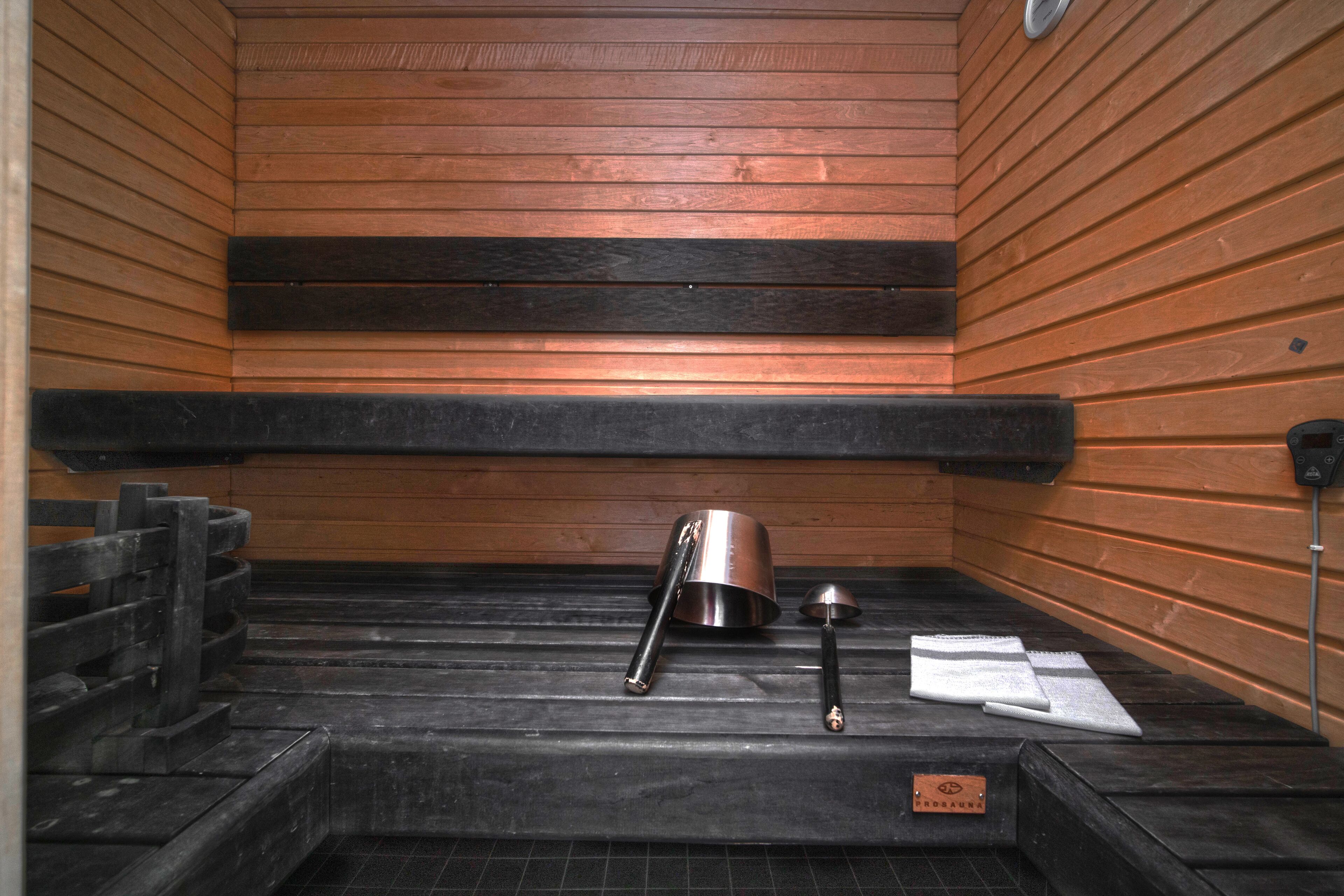 Un cuarto de sauna con paredes de madera, un banco, un balde de metal y una toalla.