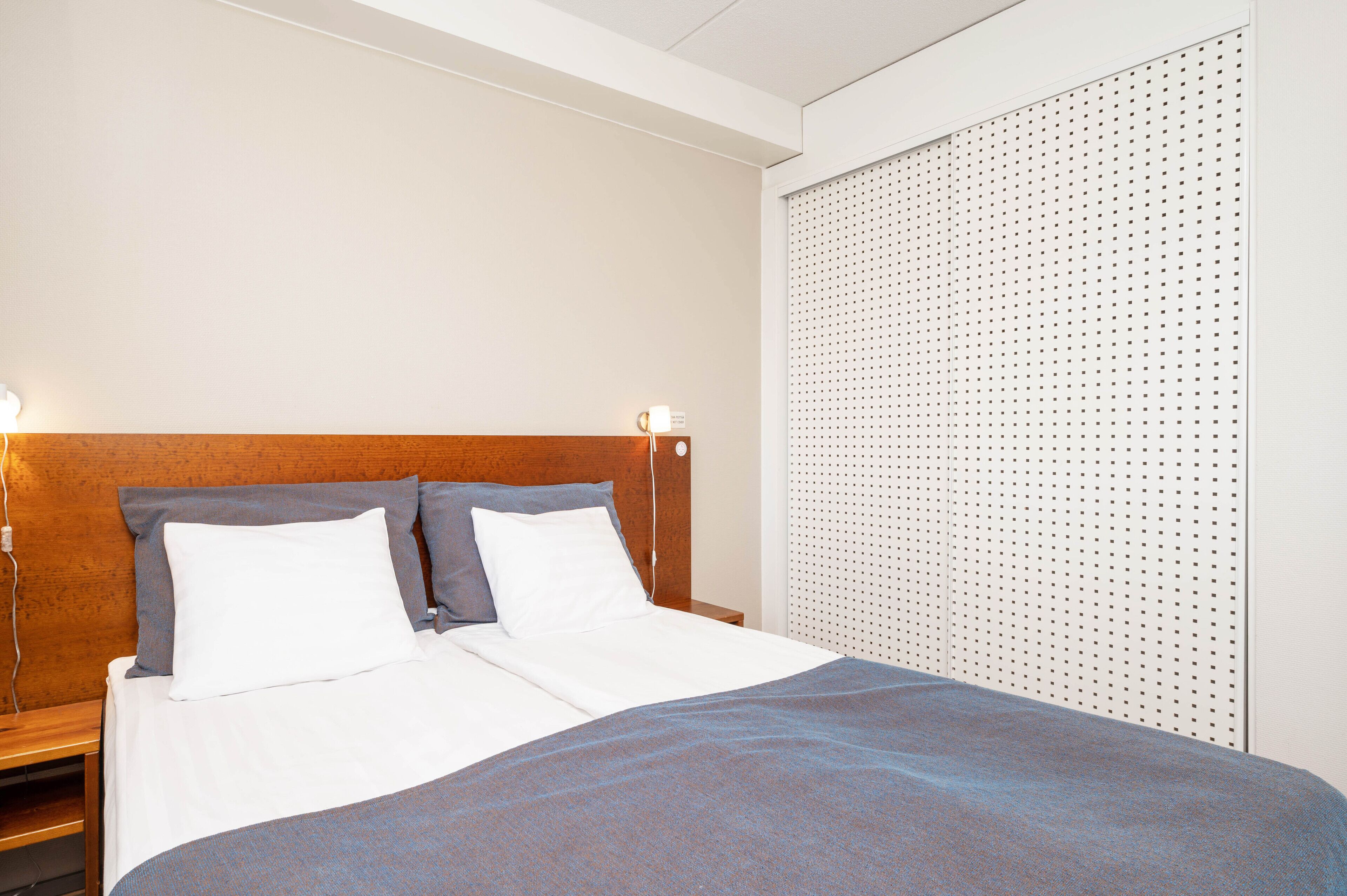 Una cama bien hecha con ropa blanca y gris, un cabecero de madera y una pared con diseño de panel perforado.