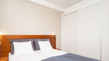 Una cama bien hecha con ropa blanca y gris, un cabecero de madera y una pared con diseño de panel perforado.