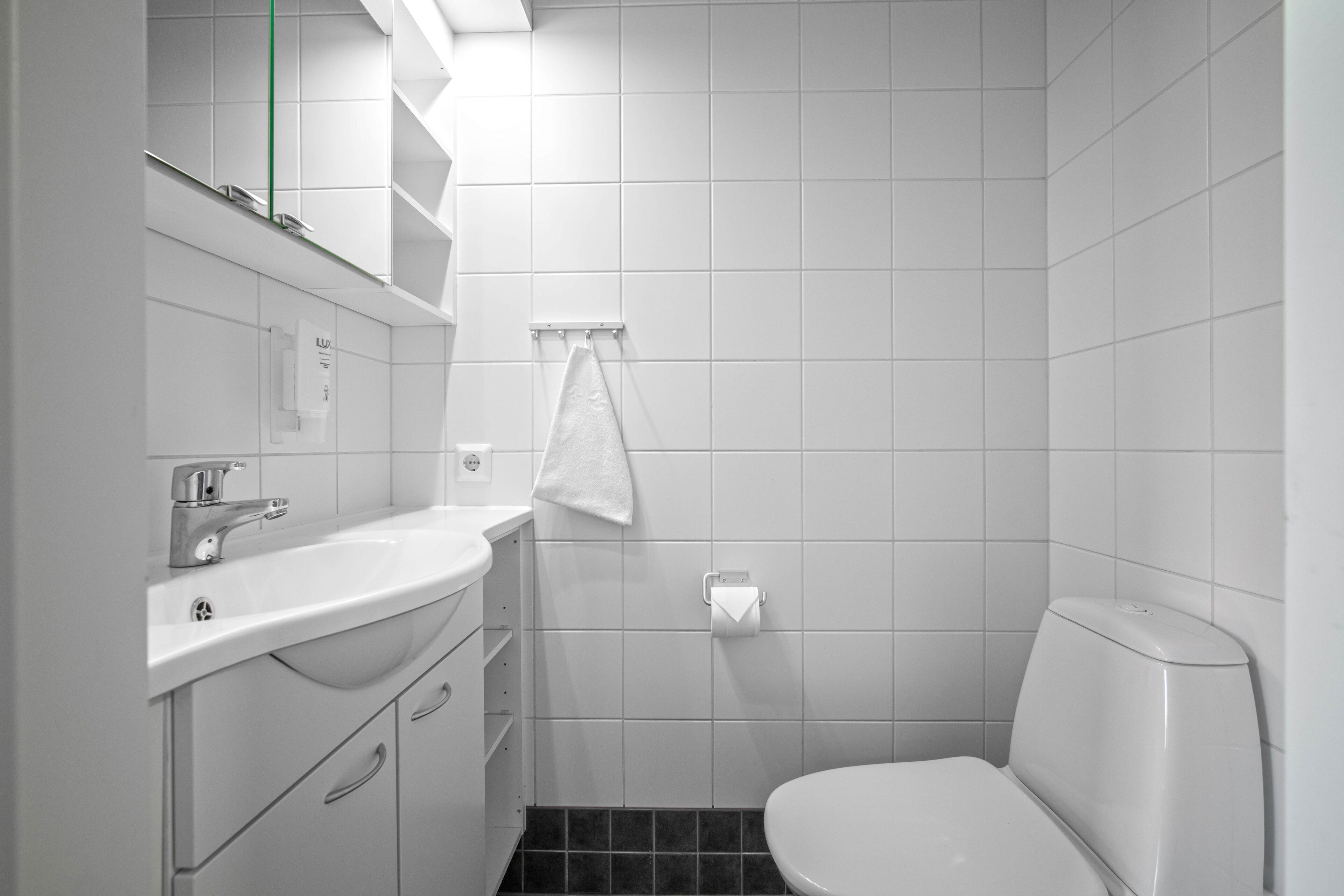 A modern bathroom with a white sink, mirror, and toilet.
