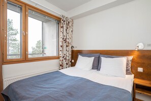 A bedroom with a large bed, wooden headboard, a window with curtains, and a nightstand with a lamp.