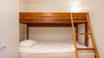 Een stapelbed met een houten trap, wit beddengoed en een witte muur.