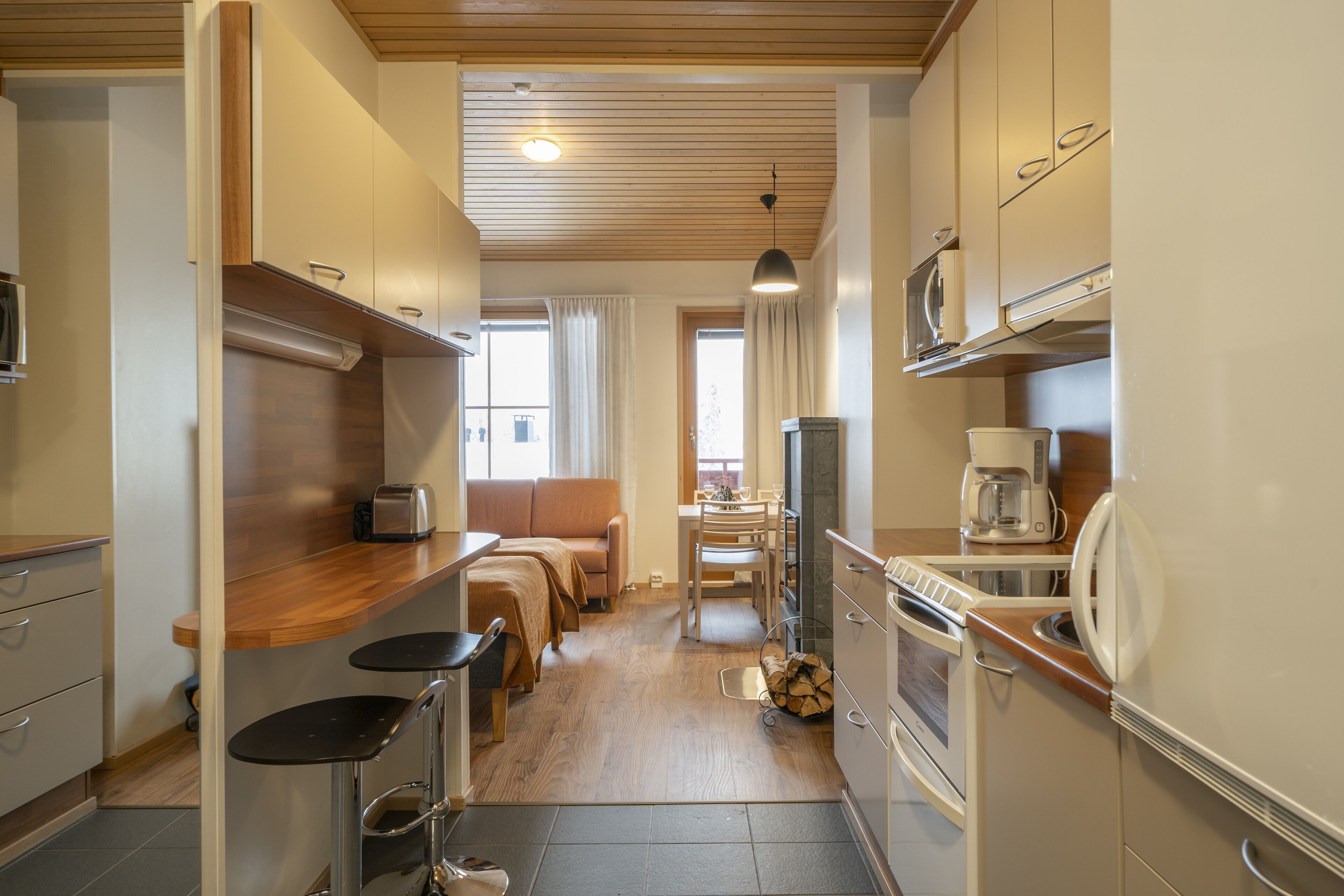 Una cucina compatta con un piano di lavoro in legno, una macchina per il caffè e un forno a microonde. C'è un'area pranzo con tavolo e sedie, e un divano.