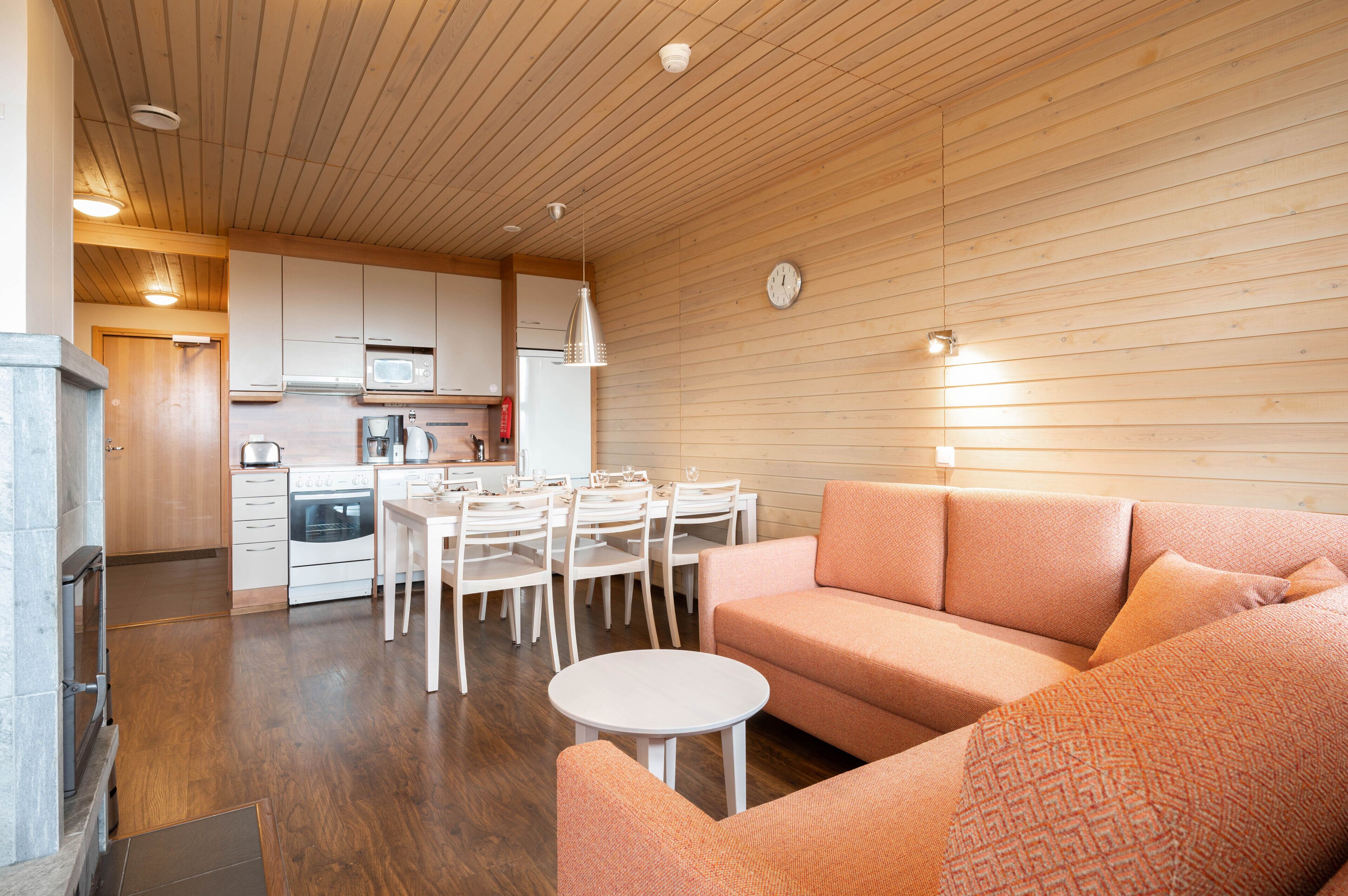 Een moderne keuken met witte kastjes, een eethoek met witte stoelen en een roze bank.