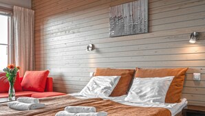 A hotel room with a wooden wall, a bed with white and orange bedding, a red sofa, and a vase with flowers. - Ski-Inn AurinkoRinne (Kuusamo)
