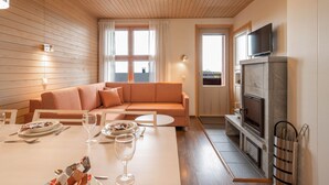A cozy living room with a sofa, a dining table set for two, and a fireplace. - Ski-Inn AurinkoRinne (Kuusamo)
