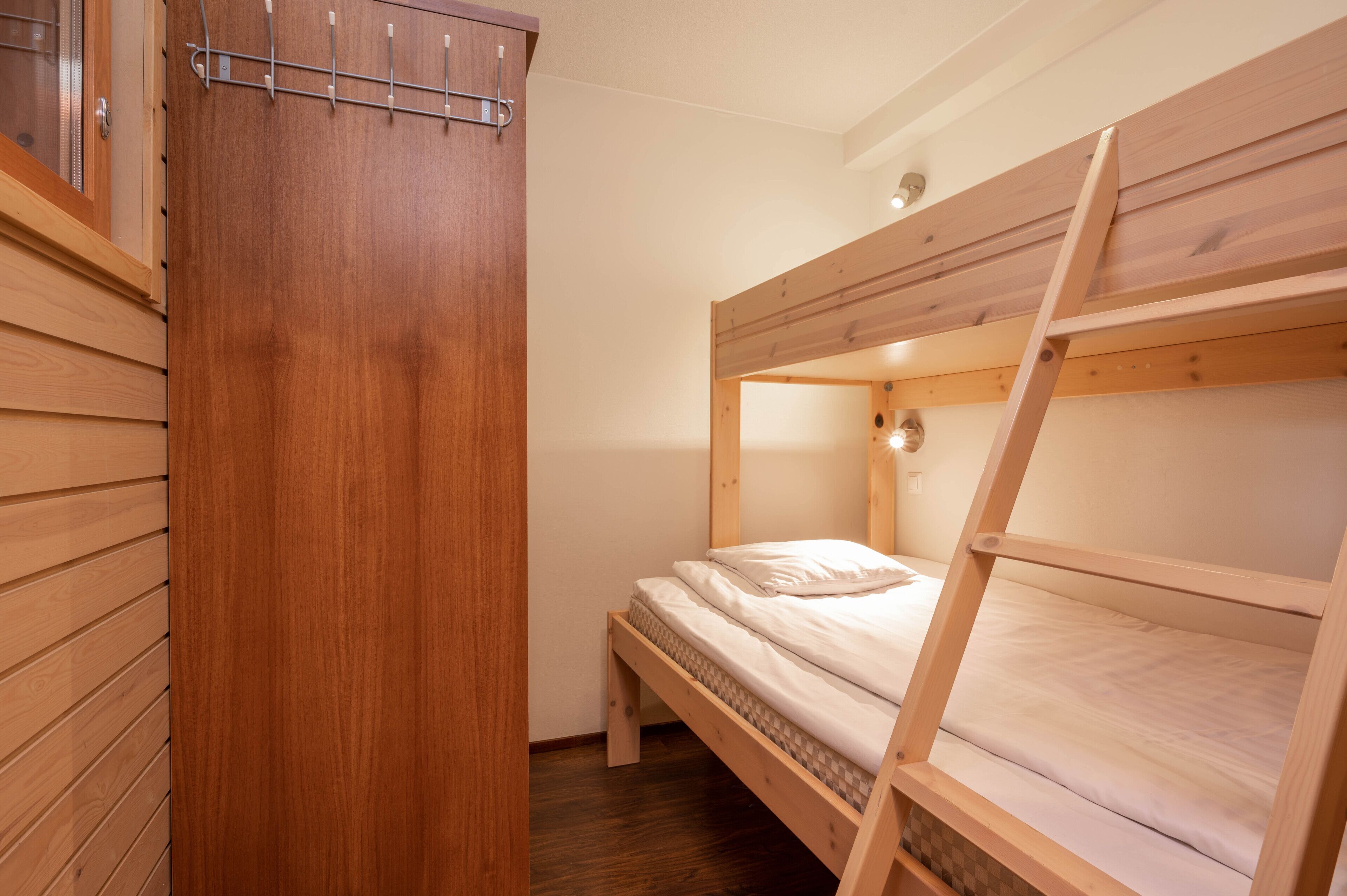 Une chambre avec un lit superposé, une armoire en bois et une petite fenêtre.