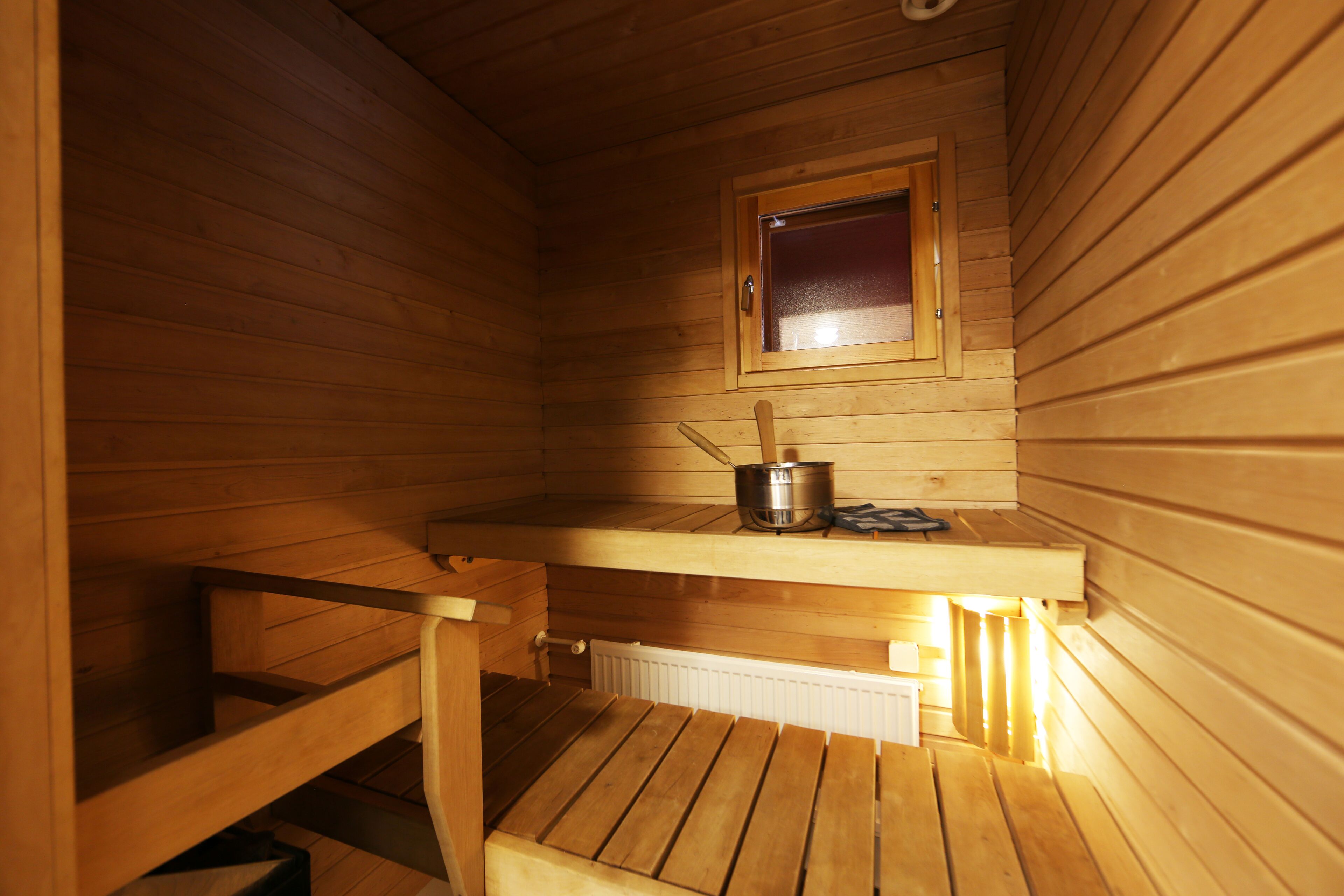 A wooden sauna with a window, a bench, and a small table with a pot.
