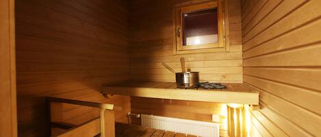 A wooden sauna with a window, a bench, and a small table with a pot.