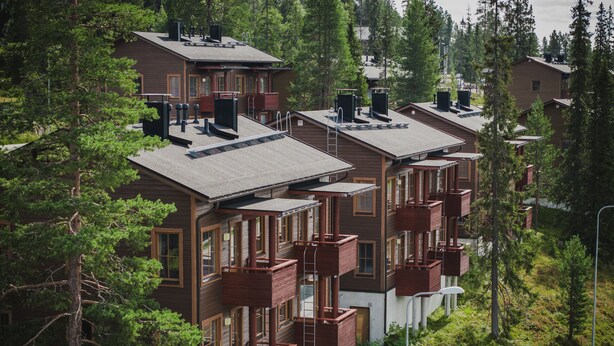 A row of modern multi-story buildings with balconies, surrounded by dense forest. - Ski-Inn AurinkoRinne (Kuusamo)