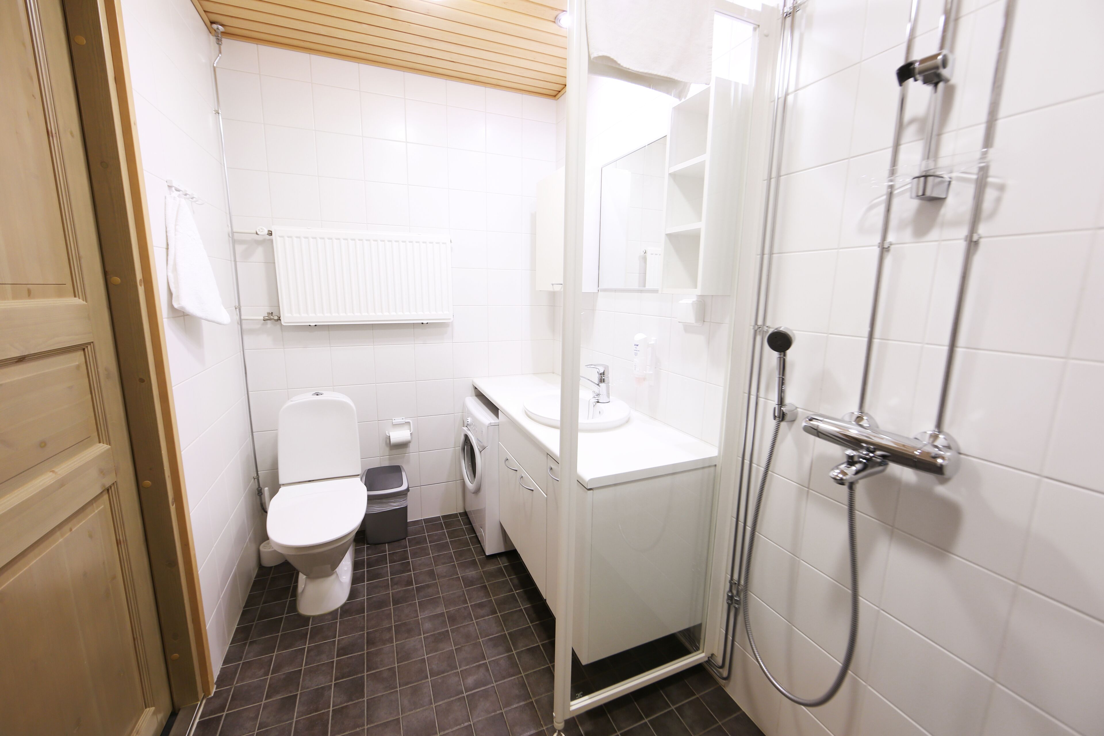 A compact bathroom with a toilet, washing machine, sink, and shower.