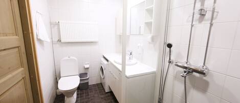 A compact bathroom with a toilet, washing machine, sink, and shower.