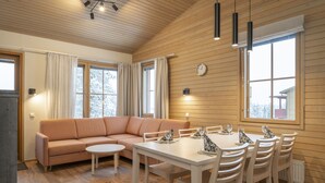 A cozy living room with a sofa, a dining table with chairs, and large windows with curtains. - Ski-Inn AurinkoRinne (Kuusamo)