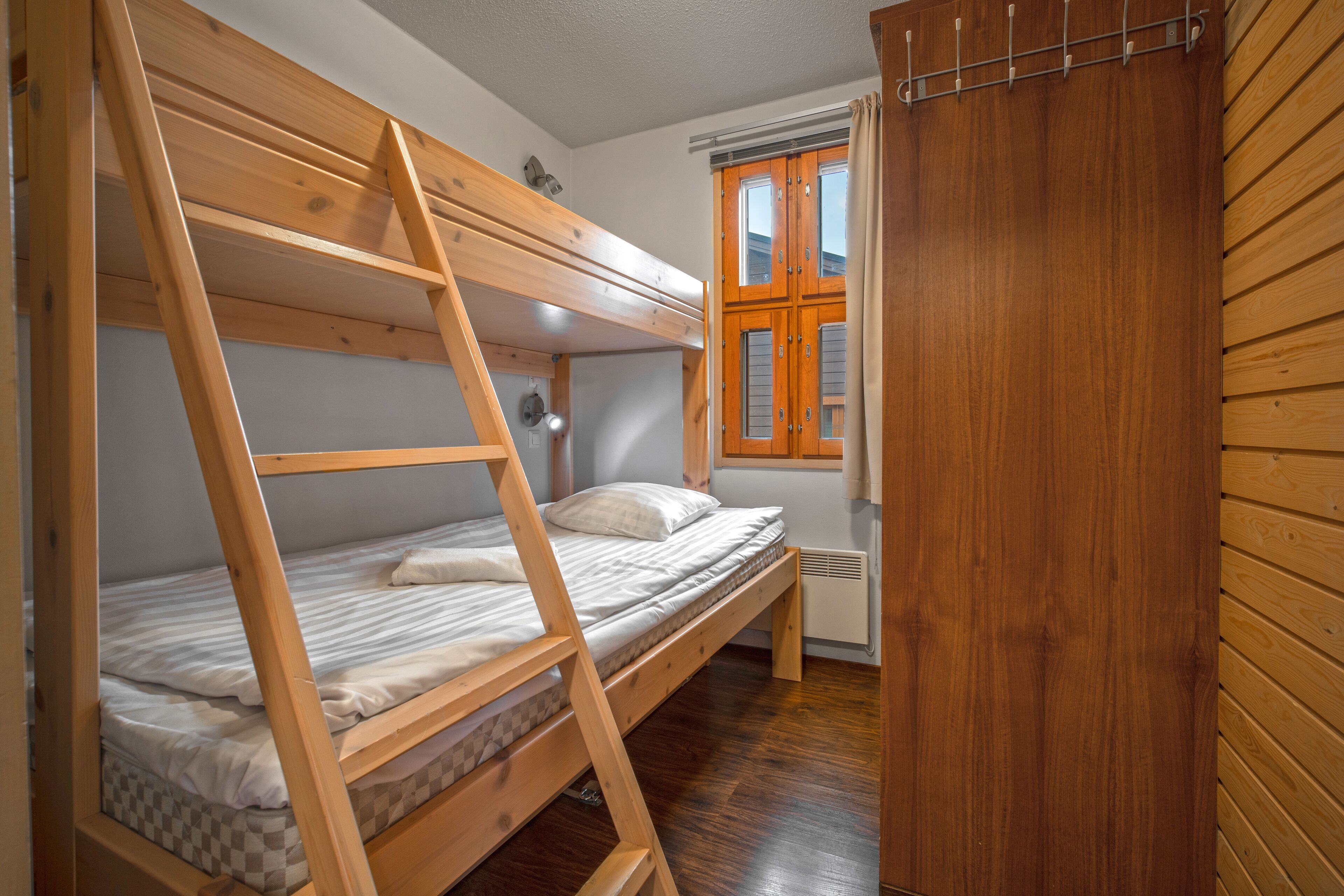 A bunk bed with a ladder, a window with curtains, and wooden walls.