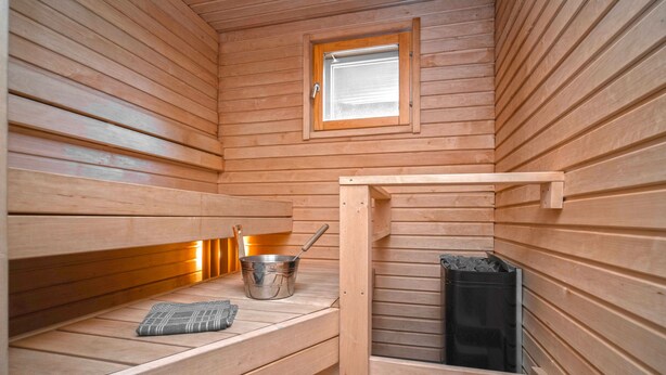 A sauna with wooden benches, a window, and a metal bucket. - Ski-Inn MastonAitio (Kuusamo)