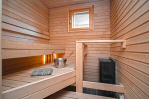 A sauna with wooden benches, a window, and a metal bucket. - Ski-Inn MastonAitio (Kuusamo)
