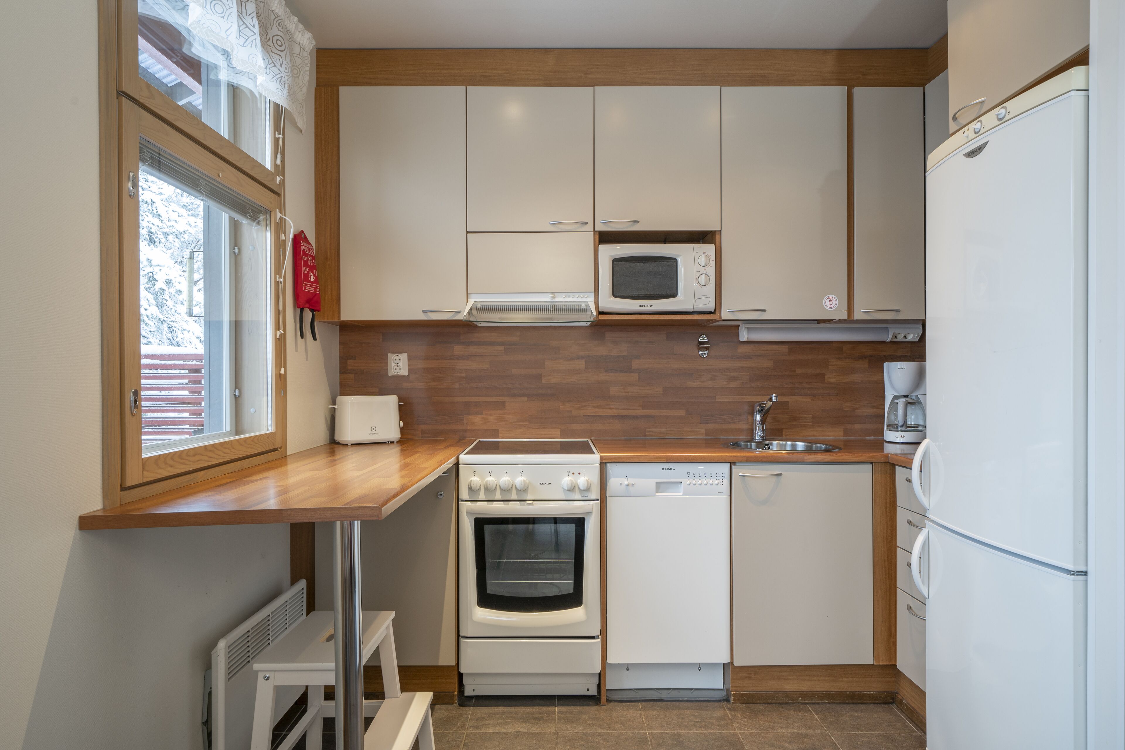 A compact kitchen with a microwave, oven, dishwasher, and a window with blinds.