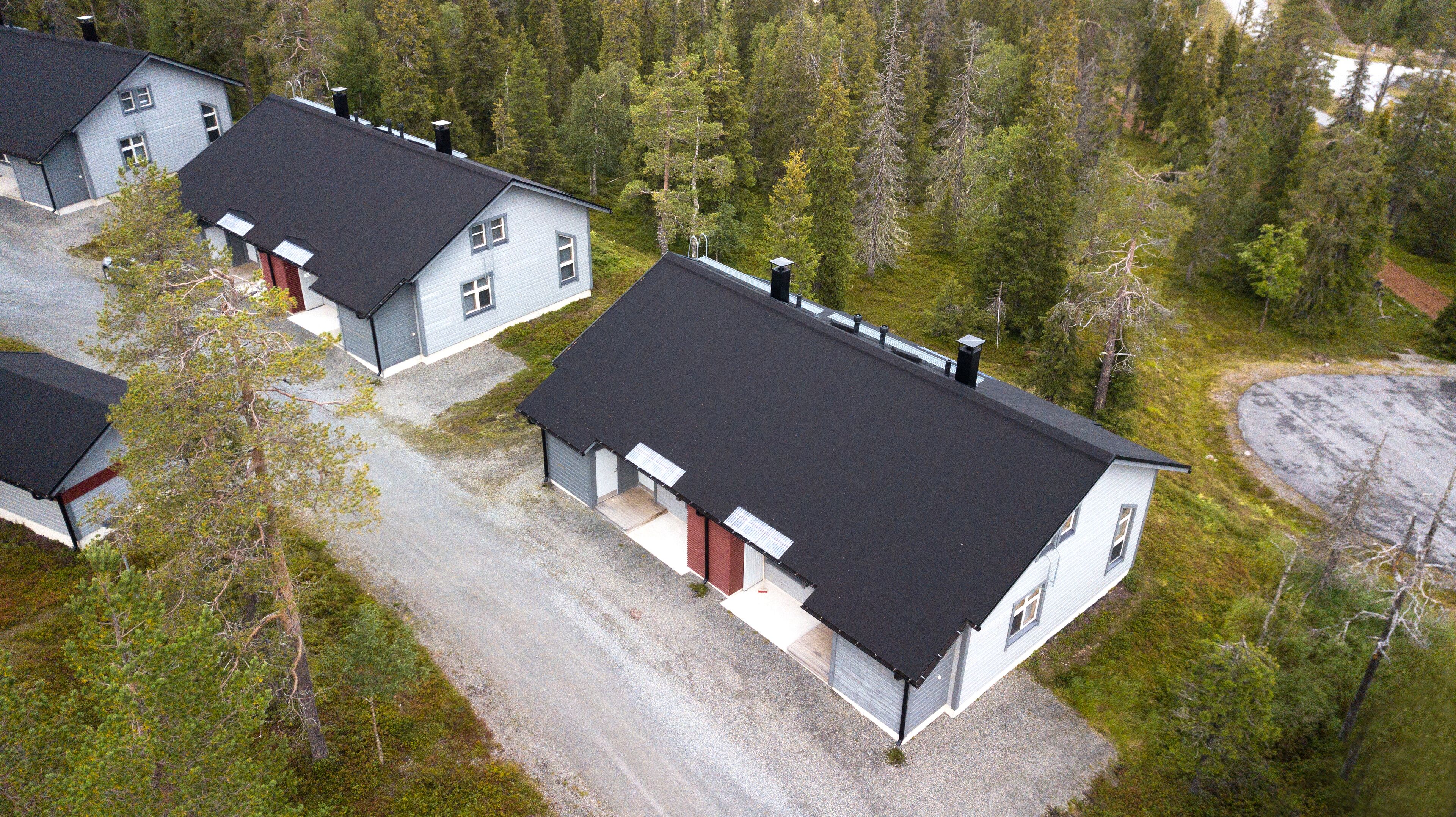 A residential area with multiple houses, each featuring a dark roof and light siding, surrounded by dense forest.