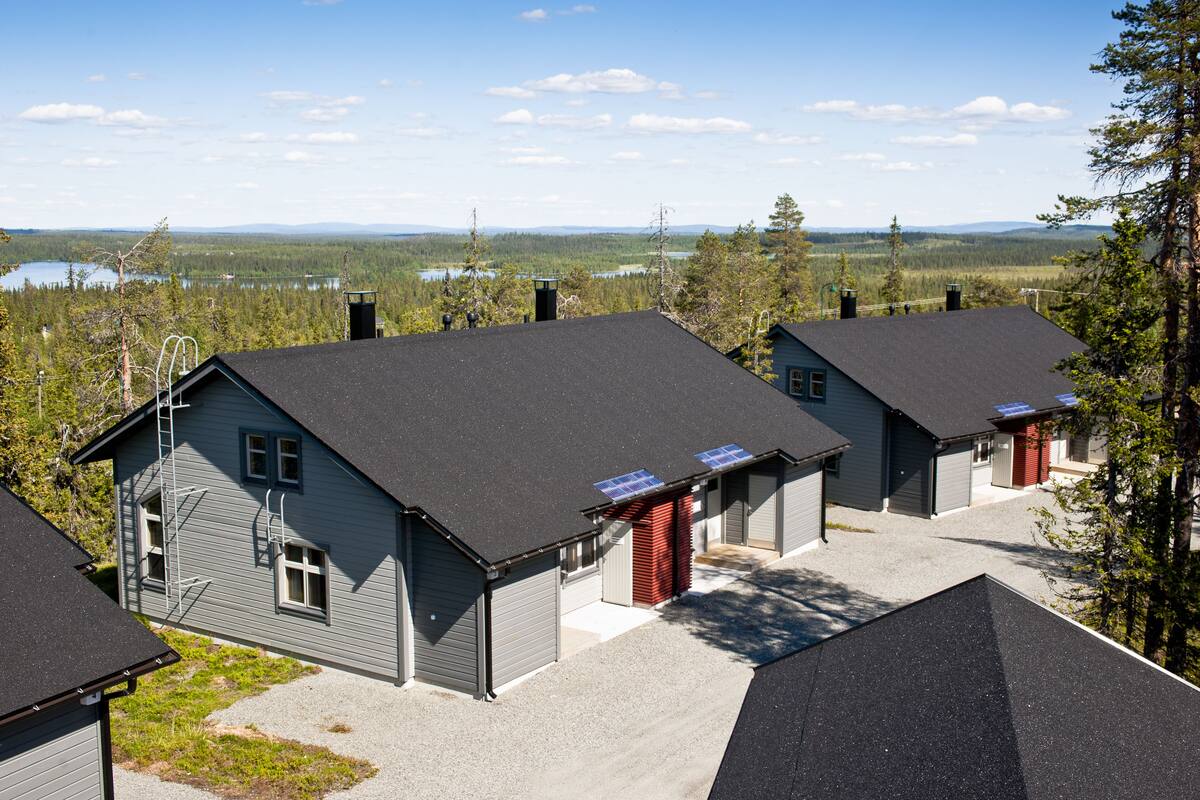 A residential area with houses featuring dark roofs and solar panels, surrounded by trees and a distant lake.