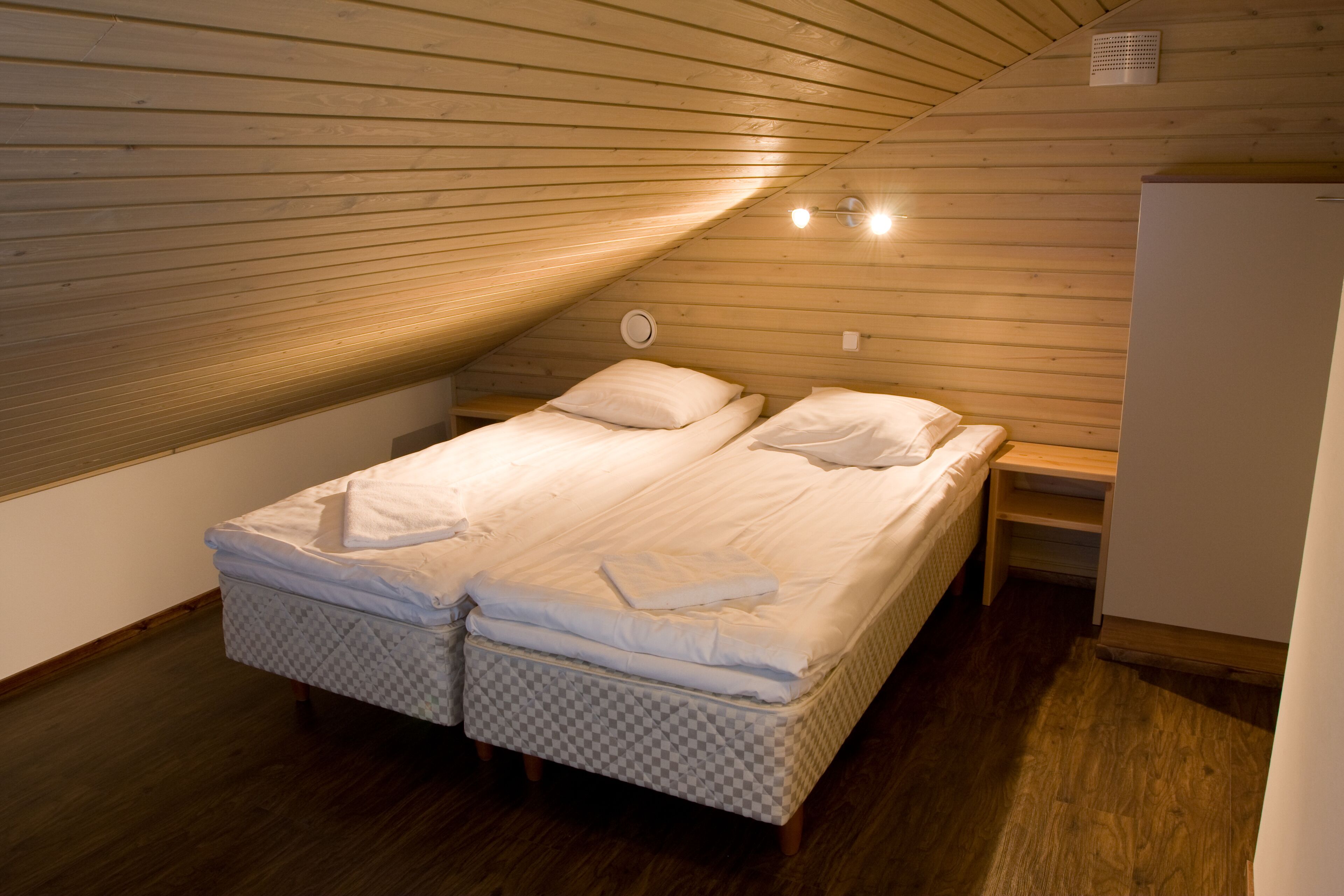 Un dormitorio con dos camas, paredes de madera, techo inclinado y un armario blanco.