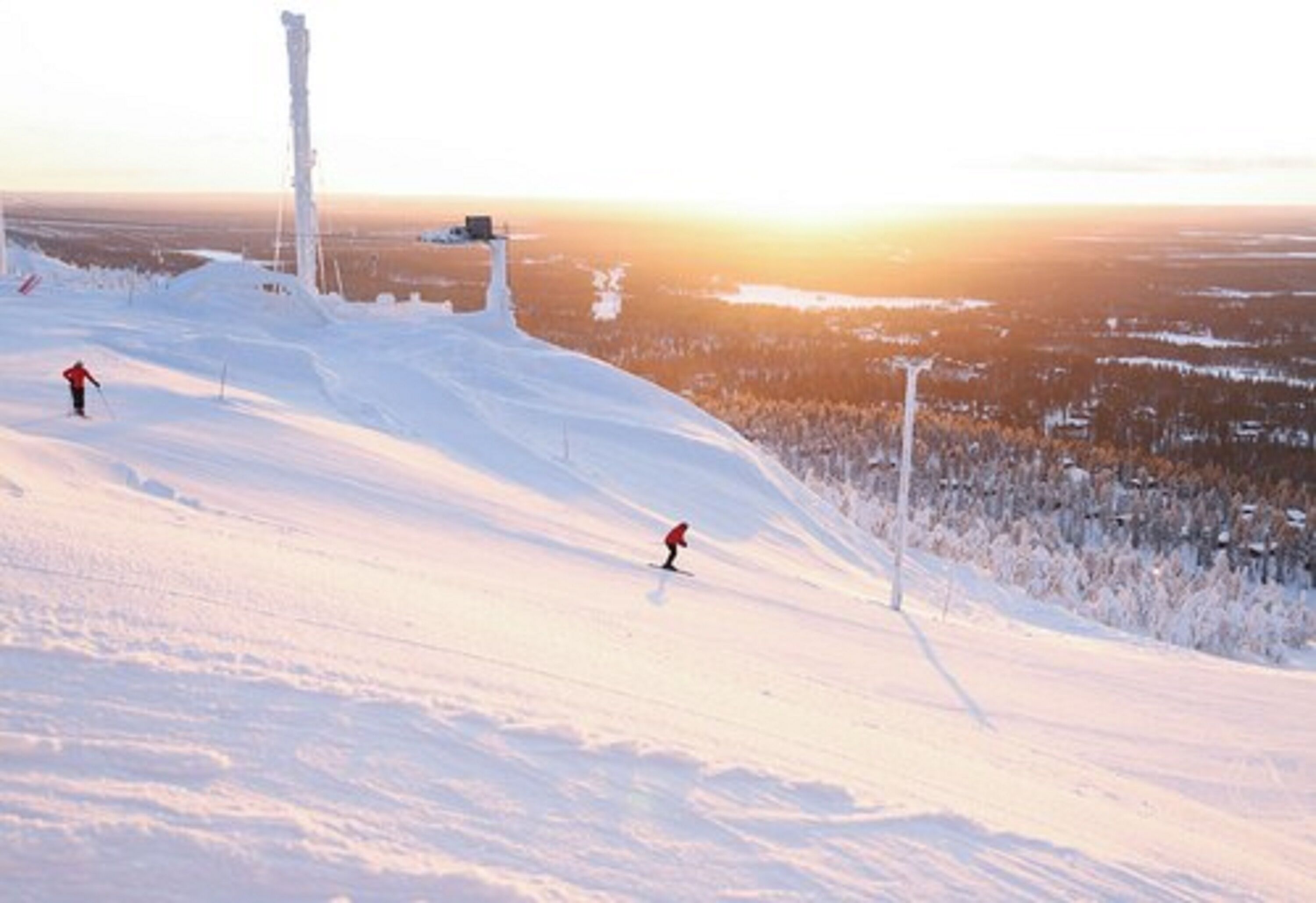 A snowy ski slope with two skiers and a tall structure in the background.