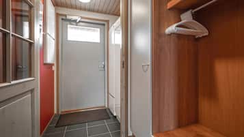 Een gang met een houten vloer, een witte deur met een raam, en een houten garderobe met kledingroede.