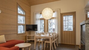 A cozy room with wooden walls, a dining table with chairs, a TV, and a fireplace. - Ski-Inn MastonAitio (Kuusamo)