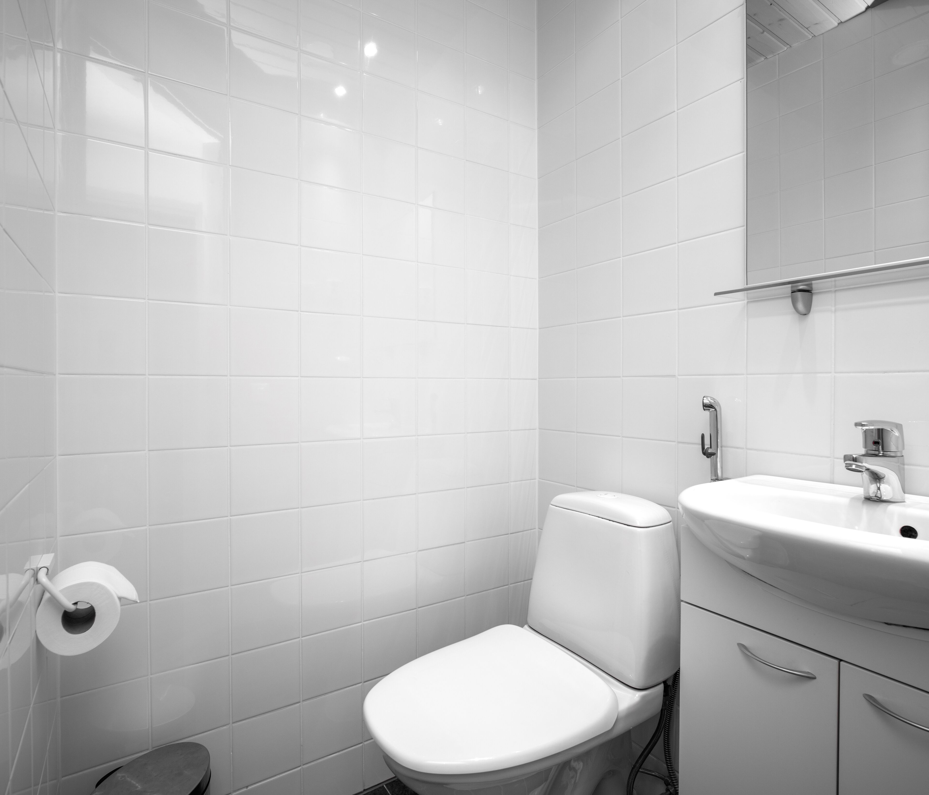 A modern bathroom with white tiles, a toilet, a sink, and a mirror.