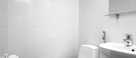 A modern bathroom with white tiles, a toilet, a sink, and a mirror.