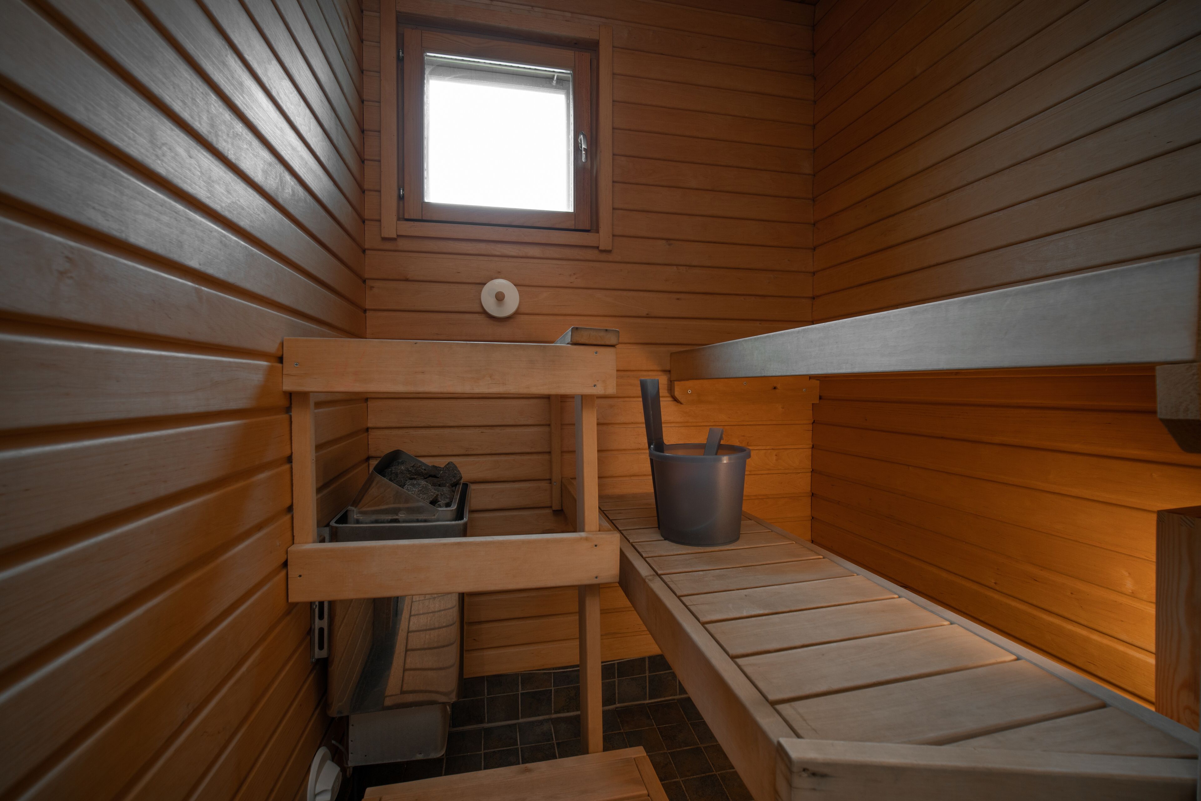 A sauna room with wooden benches, a window, and a bucket.