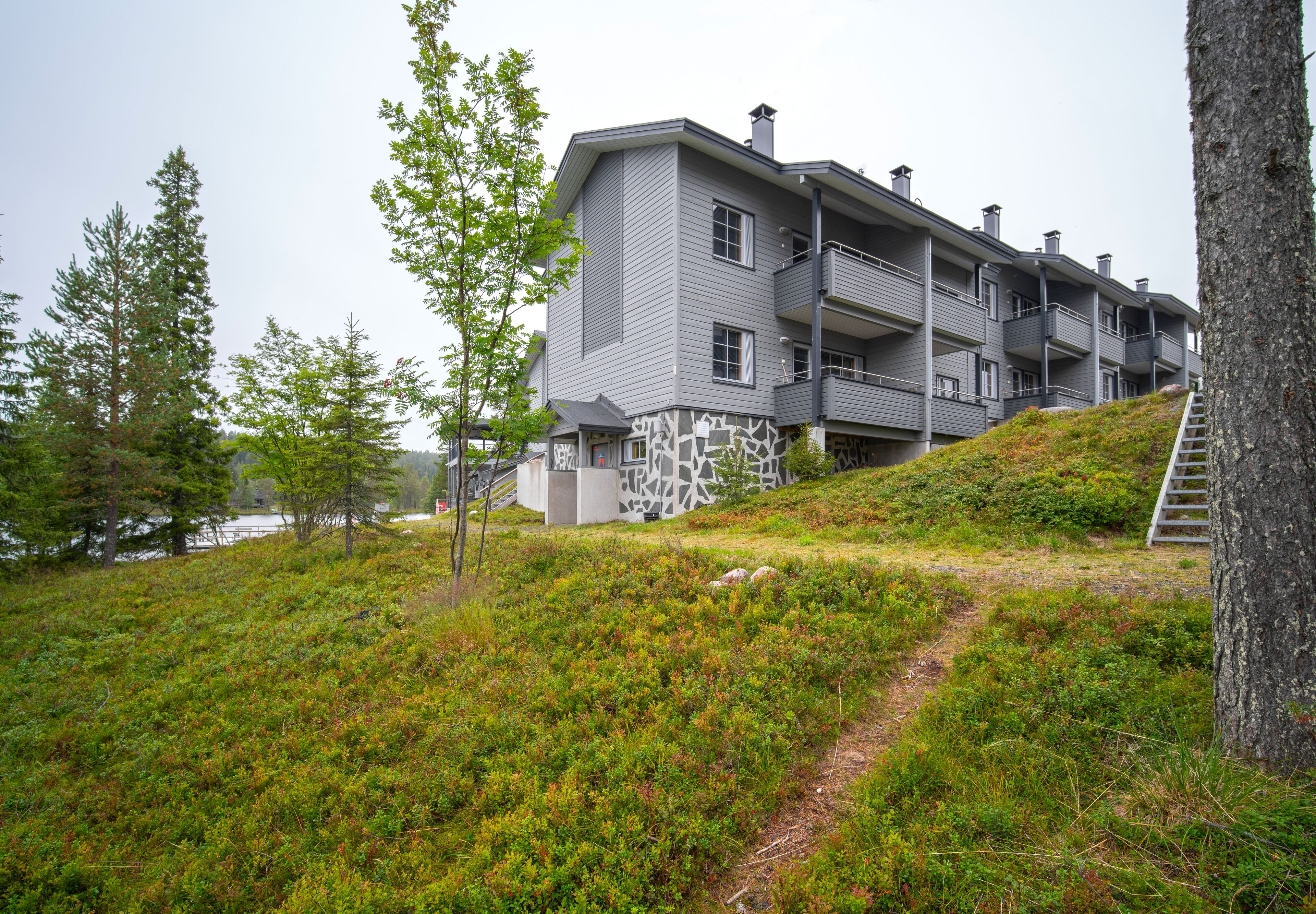 A multi-story building with balconies, situated on a hillside with a path leading to the entrance.