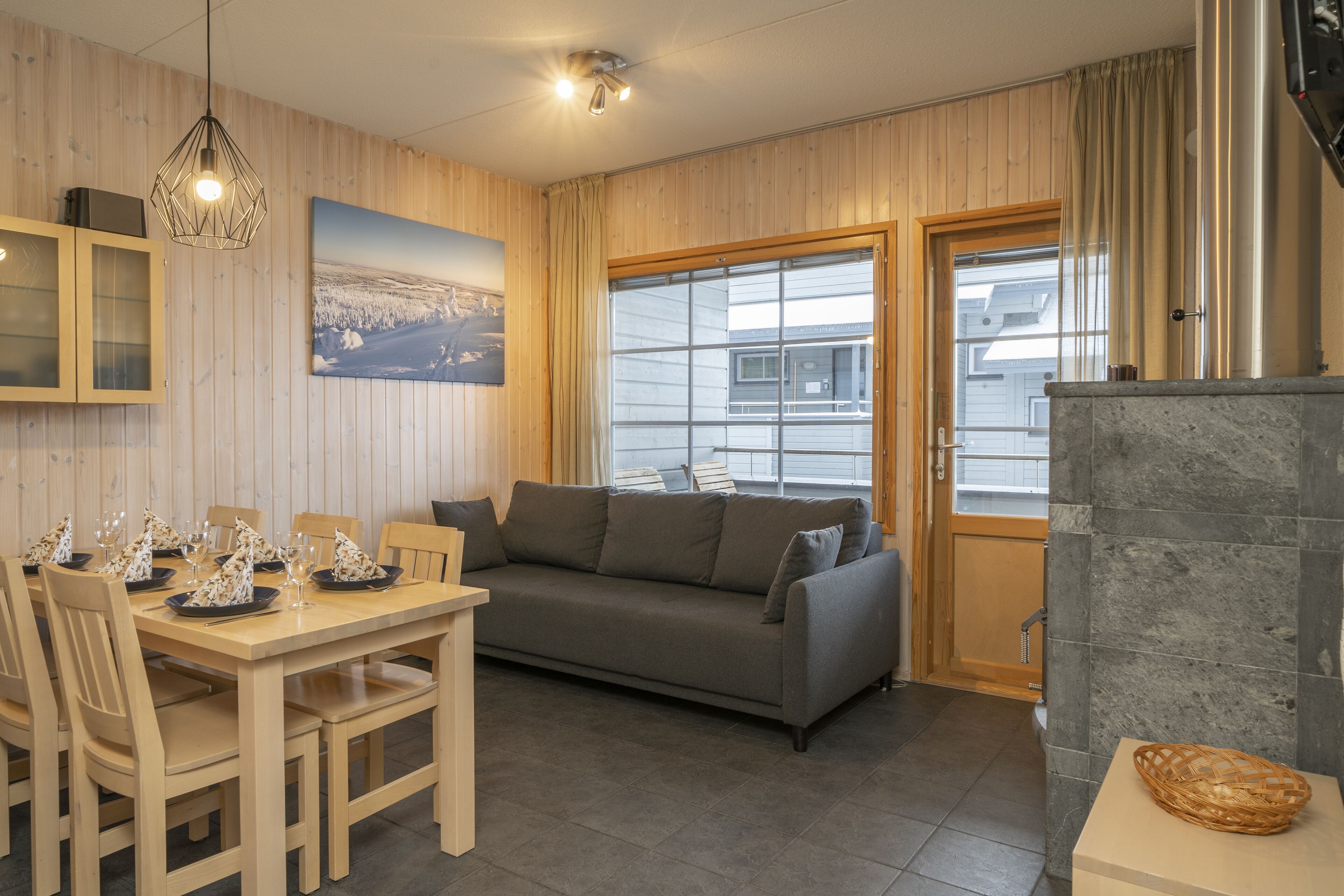 A cozy room with a wooden dining table set for a meal, a grey sofa, and a stone fireplace.